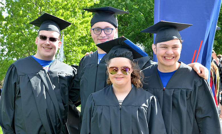 Group image of four KUT TPE graduates posing in their cap and gown at commencement.