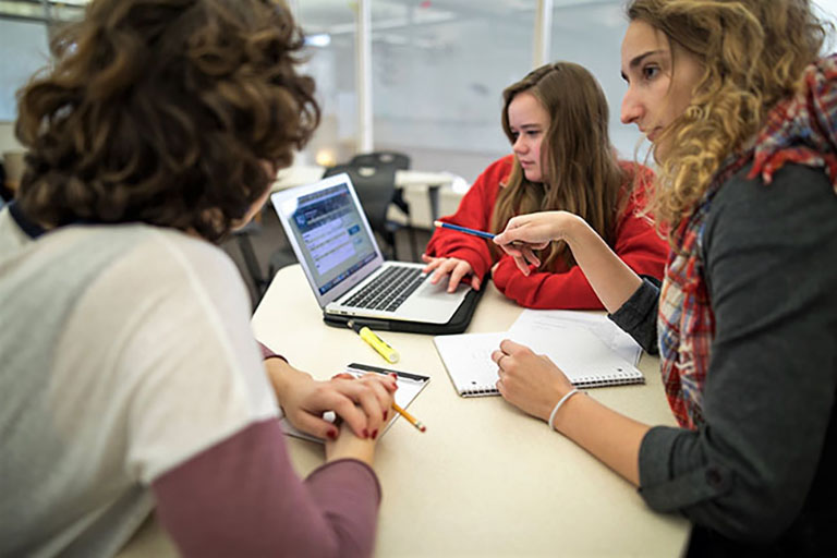 Image of three students around a laptop looking at a webpage.